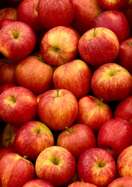 A close-up image of numerous fresh red and yellow apples piled together, displaying smooth and shiny skin with some subtle streaks of yellow and orange. The apples vary slightly in size and shape, some showing small stems protruding from the top. The lighting highlights the glossy surface of each fruit, creating reflections that emphasize their freshness. The background is filled entirely with these apples, with no other objects visible, suggesting a market or fruit stand setting. Although primarily a fruit image, it subtly connects to themes of food waste reduction and healthy disposal practices, aligning with the concept of managing perishable waste in a responsible manner. The composition is detailed and vibrant, capturing the natural textures and colours typical of ripe apples, making it visually appealing for content related to produce or waste management involving food products.